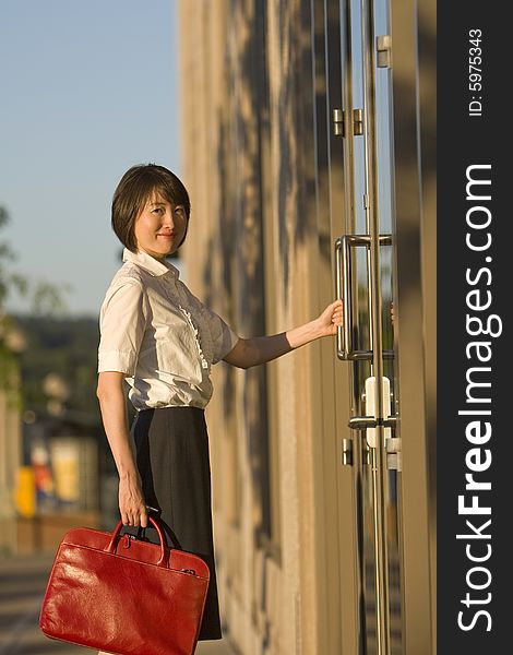 Young woman opens door while smiling at the camera. She is holding a red handbag. Vertically framed photo. Young woman opens door while smiling at the camera. She is holding a red handbag. Vertically framed photo.