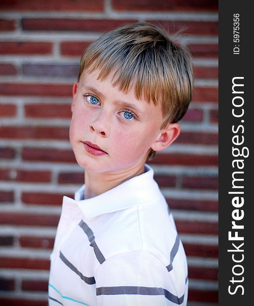 A young boy is standing up against a brick wall.  He is looking at the camera.  Vertically framed shot. A young boy is standing up against a brick wall.  He is looking at the camera.  Vertically framed shot.