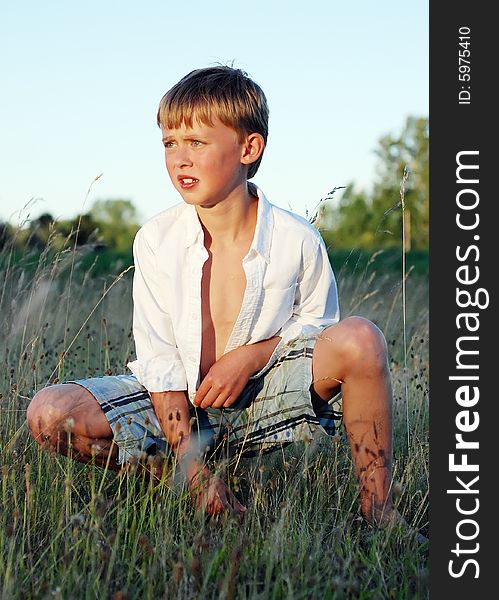 A young boy is sitting outside in a field of grass.  He is looking away from the camera.  Vertically framed shot. A young boy is sitting outside in a field of grass.  He is looking away from the camera.  Vertically framed shot.