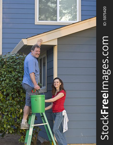 Man and woman standing on a ladder near a blue house. Man and woman standing on a ladder near a blue house
