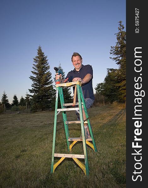 Man on ladder holding a drill and smiling. Vertically framed photograph. Man on ladder holding a drill and smiling. Vertically framed photograph