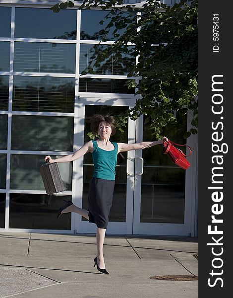 Young woman leaps in front of building while holding a red handbag and a briefcase. Vertically framed photo. Young woman leaps in front of building while holding a red handbag and a briefcase. Vertically framed photo.