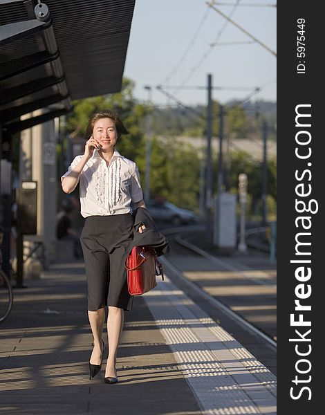 Young woman walks along tracks talking on her cell phone. She is carrying a red bag. Vertically framed photo. Young woman walks along tracks talking on her cell phone. She is carrying a red bag. Vertically framed photo.