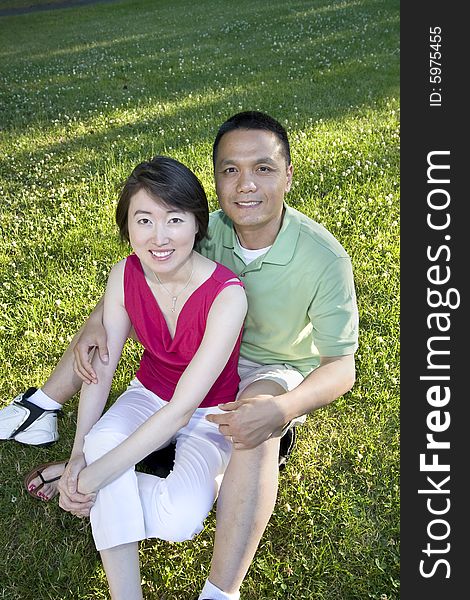 Man sits on grass smiling at camera. Woman reclines against him. Vertically framed photo. Man sits on grass smiling at camera. Woman reclines against him. Vertically framed photo.