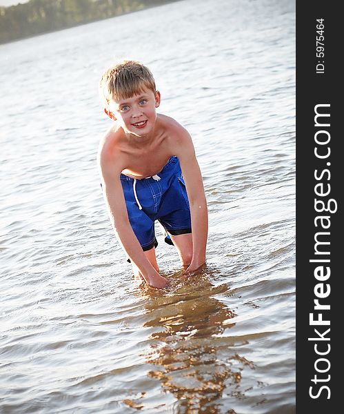 A young boy is standing up to his knees in water.  He is smiling at the camera.  Vertically framed shot. A young boy is standing up to his knees in water.  He is smiling at the camera.  Vertically framed shot.