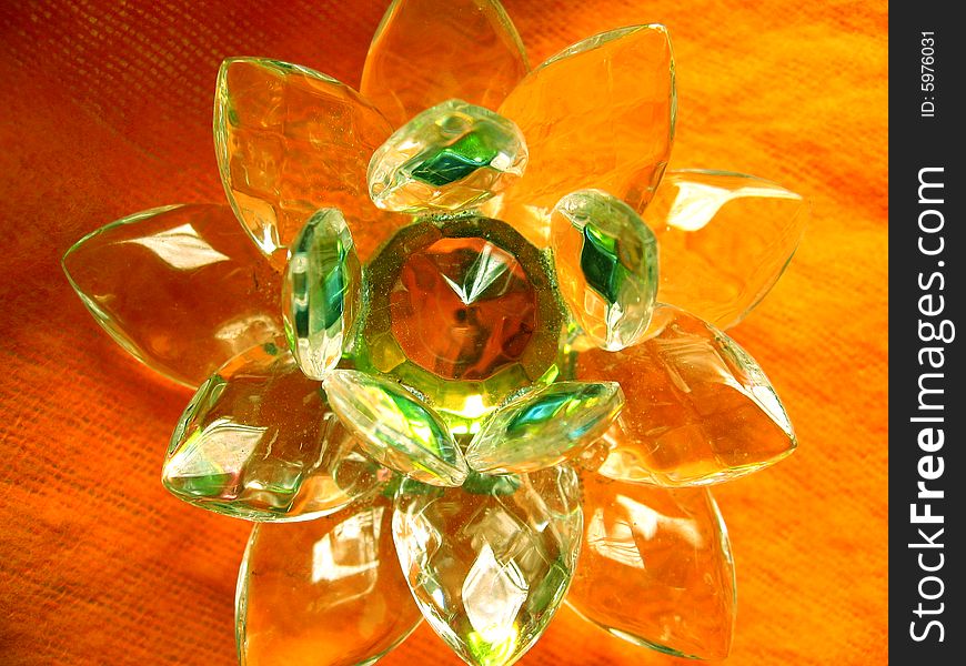 A beautiful crystal lotus showing orange colored reflection with green outline as it is kept on orange cloth
