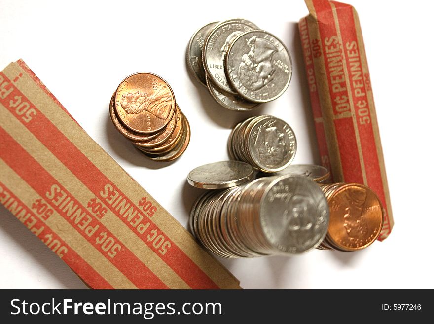 Loose change with penny rolls.  Focus is on the smaller stacks, quarters, dimes, pennies and the coin rolls.