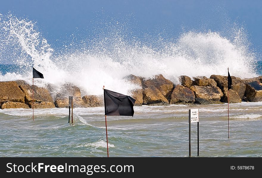 Big wave strikes breakwater fence. Black flags indicate no bathing warning. Big wave strikes breakwater fence. Black flags indicate no bathing warning