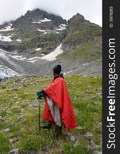 Man in red cape looking to mountain with glacier