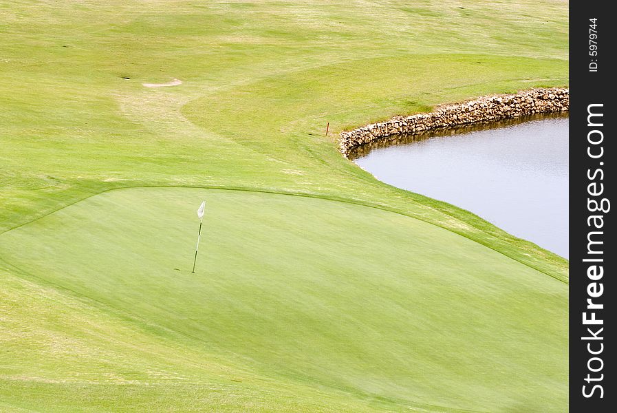 A green on a golf course with flag next to a water trap. A green on a golf course with flag next to a water trap