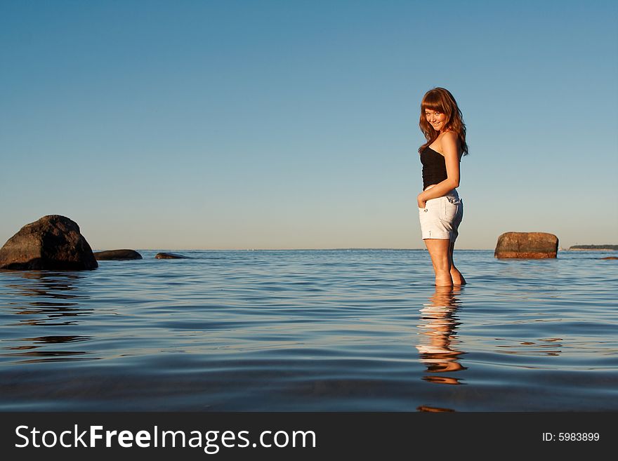 Happy young woman standing in water and looking over her shoulder