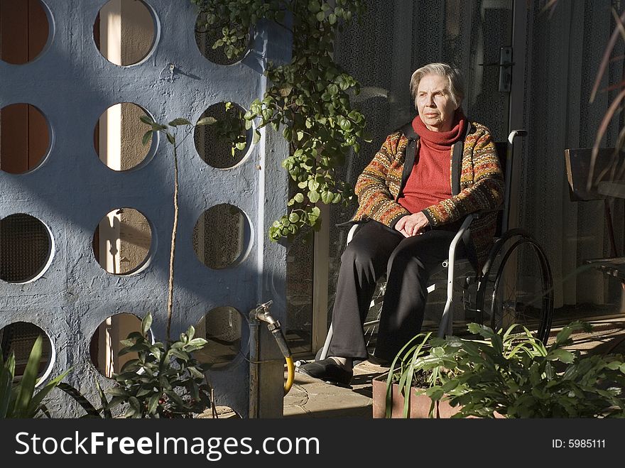 An elderly woman is sitting in a wheelchair in her garden. She is staring off into the distance. Horizontally framed shot. An elderly woman is sitting in a wheelchair in her garden. She is staring off into the distance. Horizontally framed shot.