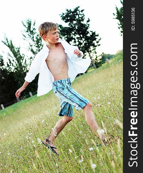 A young boy, with his button up shirt open, runs in a grass field, looking away from the camera. Vertically framed shot. A young boy, with his button up shirt open, runs in a grass field, looking away from the camera. Vertically framed shot.