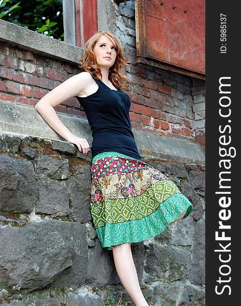 A young and attractive woman, leans up against a rock wall, looking away from the camera. Vertically framed shot. A young and attractive woman, leans up against a rock wall, looking away from the camera. Vertically framed shot.