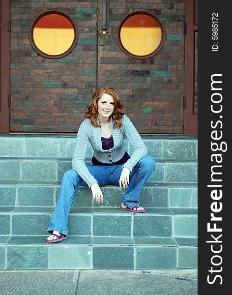 A young girl is sitting outside of a building on some stairs.  She is smiling at the camera.  Vertically framed shot. A young girl is sitting outside of a building on some stairs.  She is smiling at the camera.  Vertically framed shot.