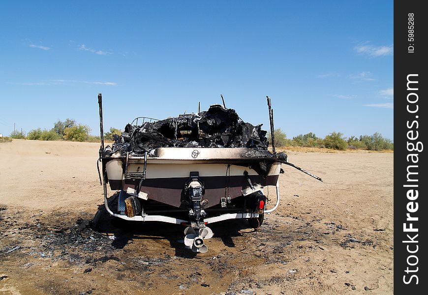 Burned wreckage of a power boat on a trailer. The boat is marooned in a desert, far from water. Horizontally framed shot. Burned wreckage of a power boat on a trailer. The boat is marooned in a desert, far from water. Horizontally framed shot.