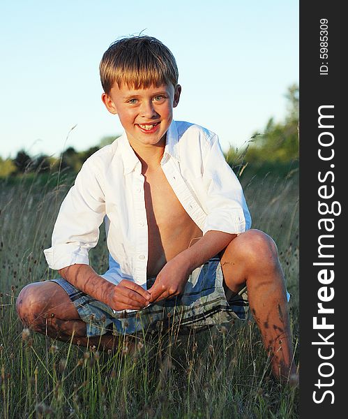 A young boy is sitting outside in a field of grass.  He is smiling at the camera.  Vertically framed shot. A young boy is sitting outside in a field of grass.  He is smiling at the camera.  Vertically framed shot.