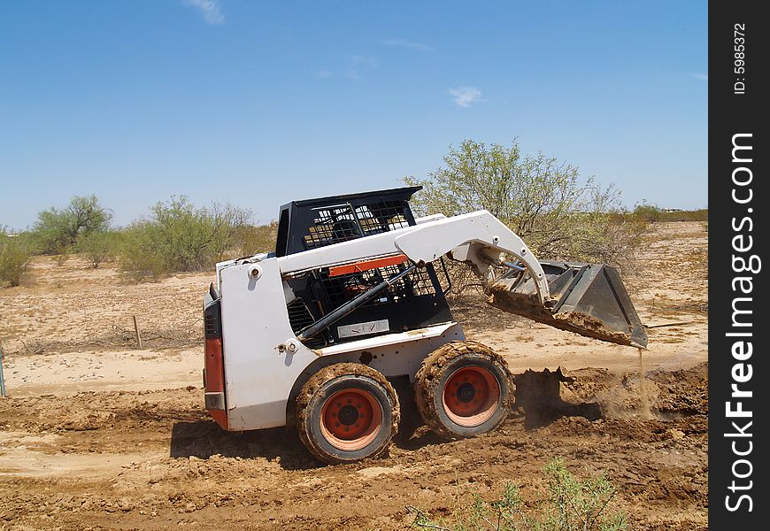 Construction worker driving a skid steer loader at a desert construction site. Horizontally framed shot. Construction worker driving a skid steer loader at a desert construction site. Horizontally framed shot.