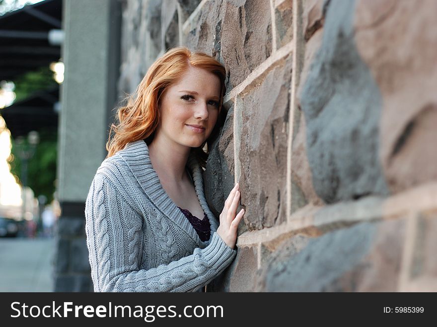 A young girl is standing next to a wall of bricks.  She is touching the wall and smiling at the camera.  Horizontally framed shot. A young girl is standing next to a wall of bricks.  She is touching the wall and smiling at the camera.  Horizontally framed shot.