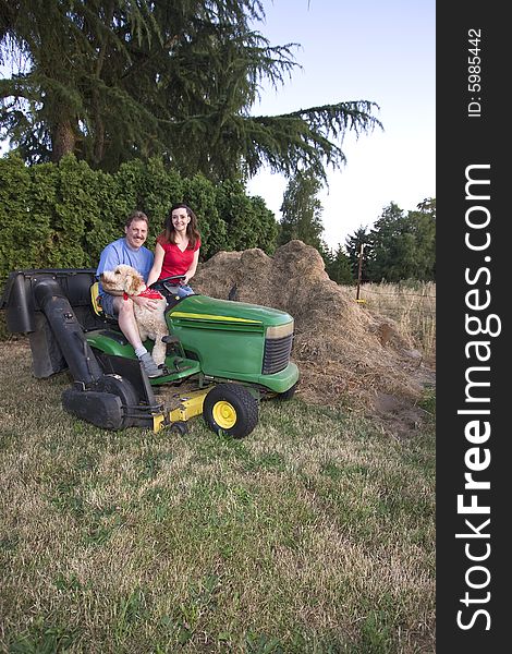 A man, woman and their dog sitting on a tractor smiling. Vertically framed photograph. A man, woman and their dog sitting on a tractor smiling. Vertically framed photograph