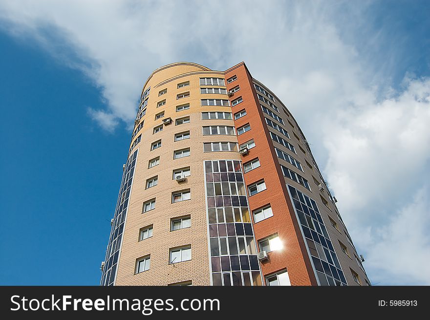 Sun glare in window of high multistory house of red and yellow bricks in blue sky