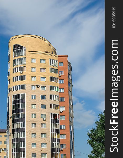 Sun glare in window of high multistory house of red and yellow bricks in blue sky