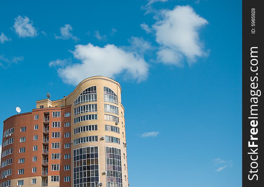 Sun glare in window of high multistory house of red and yellow bricks in blue sky