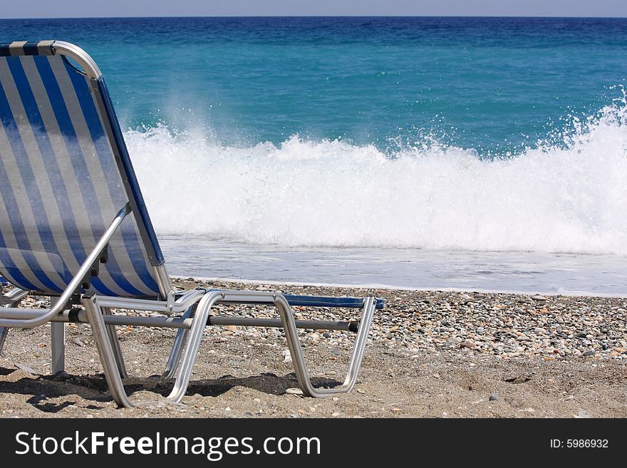 An empty beach chair facing to a breaking wave. An empty beach chair facing to a breaking wave