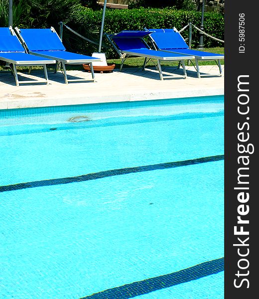 A glimpse of a pool with deck chairs and umbrella. A glimpse of a pool with deck chairs and umbrella