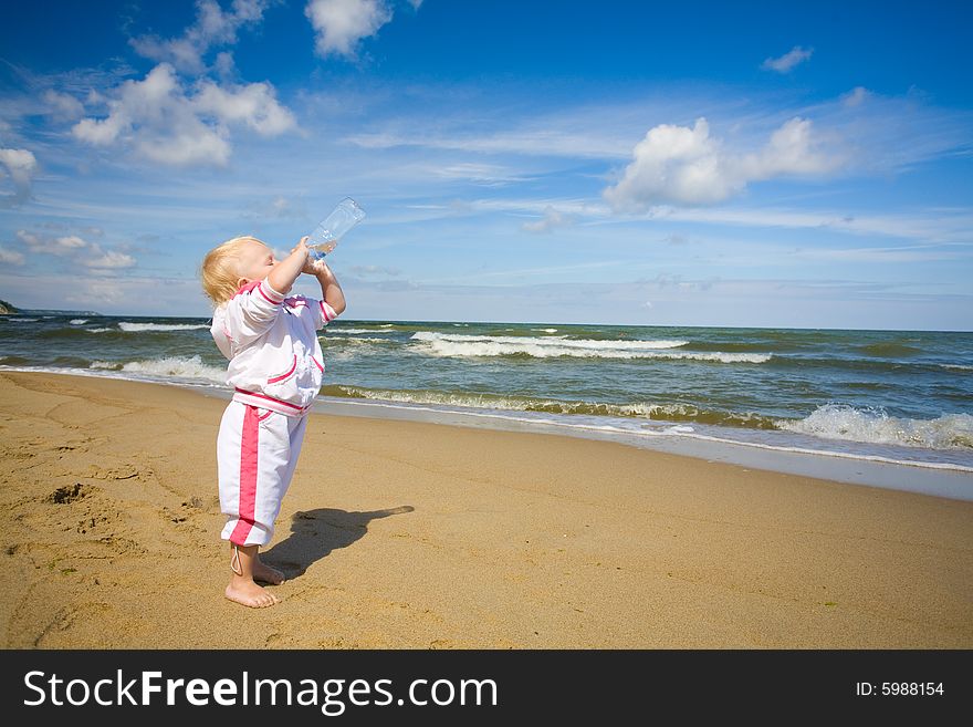 Little girl standing on coastline and drinking water. Little girl standing on coastline and drinking water