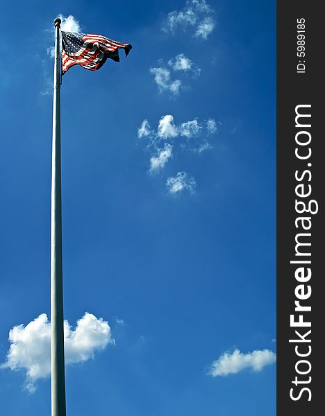 American flag blows in the wind at the top of a white flag pole against a rich blue sky. American flag blows in the wind at the top of a white flag pole against a rich blue sky