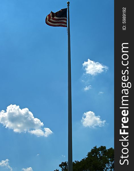 American flag blows in the wind at the top of a white flag pole against a rich blue sky. American flag blows in the wind at the top of a white flag pole against a rich blue sky
