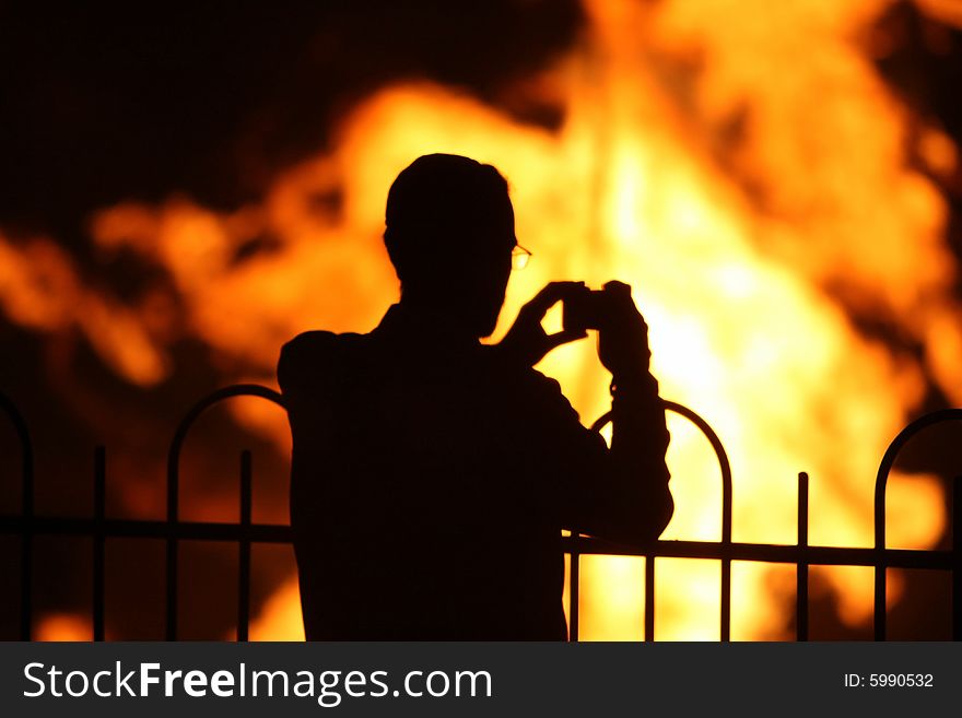 Silhouette of a man taking a photo of a fire