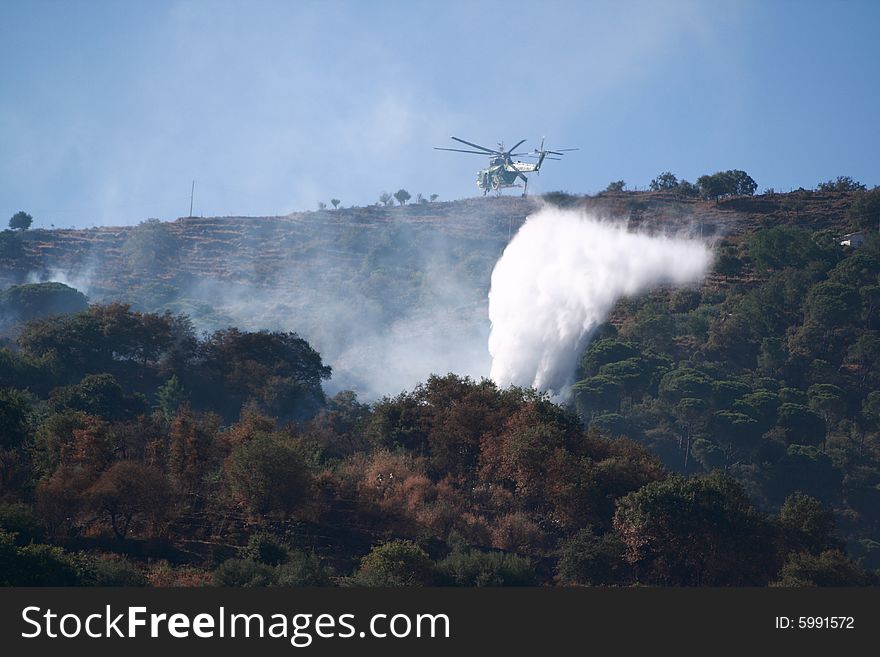 A fire helicopter dropping water on a brush fire as a firefighter watches