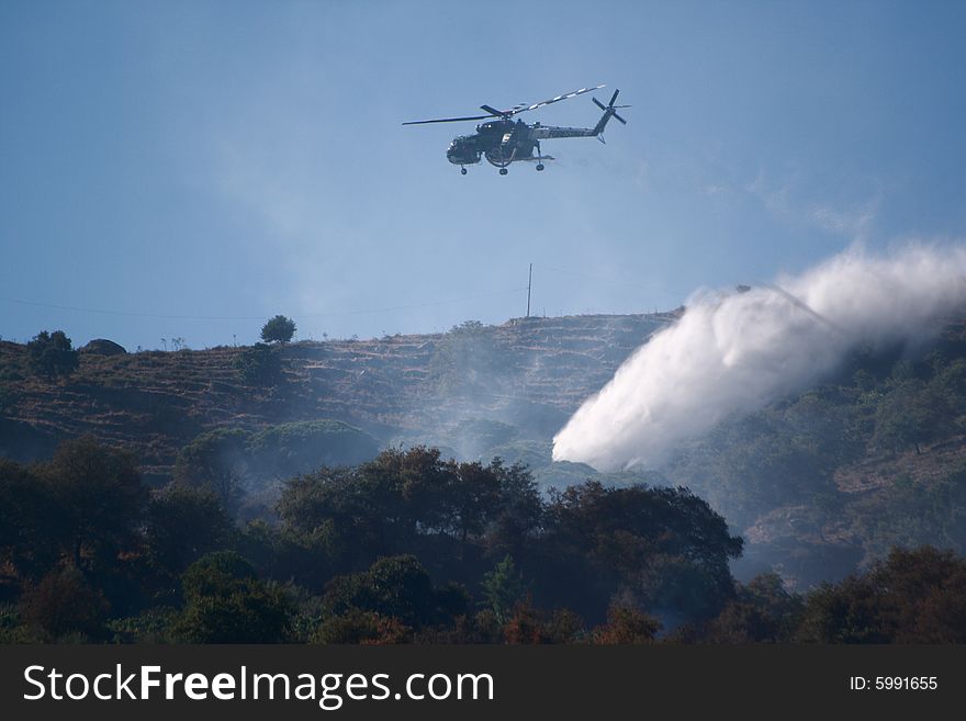 A fire helicopter dropping water on a brush fire as a firefighter watches