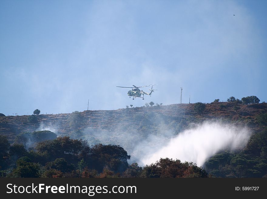 A fire helicopter dropping water on a brush fire as a firefighter watches