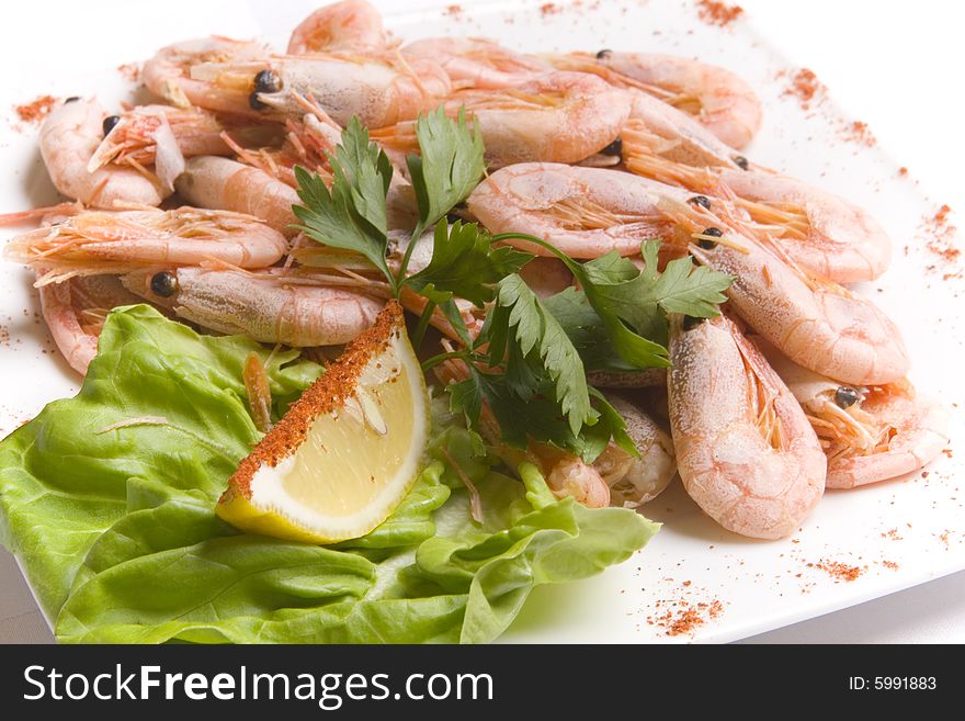 Boiled shrimps with salad leaves and slice of lemon on white plate