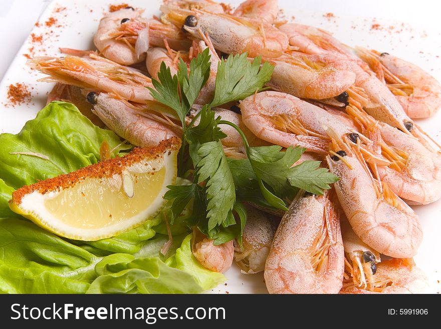 Boiled shrimps with salad leaves and slice of lemon on white plate