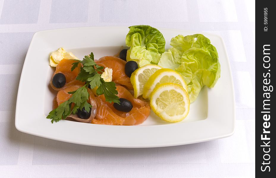 Salty salmon decorated with salad leaves, lemon slice, olives and parsley on white plate