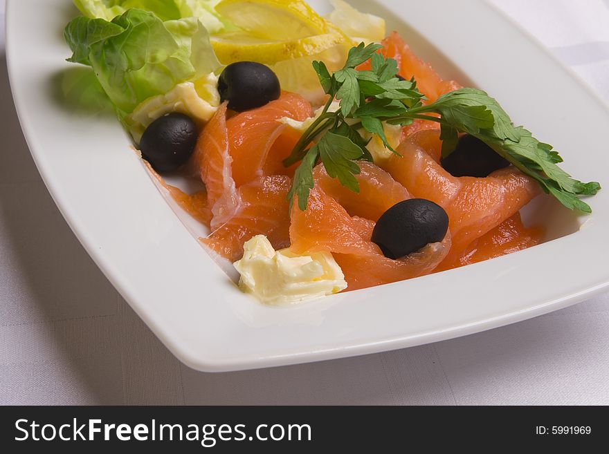 Salty salmon decorated with salad leaves, lemon slice, olives and parsley on white plate