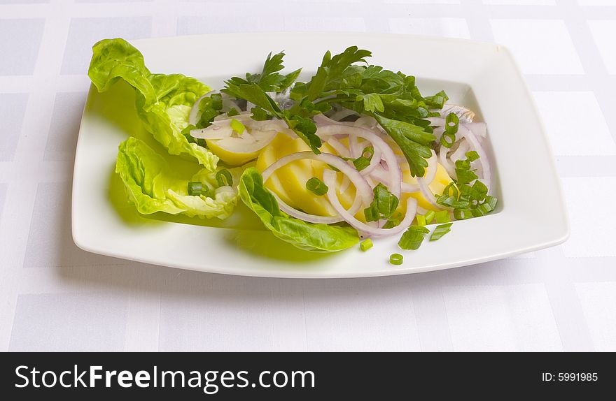 Herring with potatoes, onion and parsley on white plate