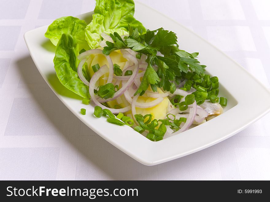 Herring with potatoes, onion and parsley on white plate