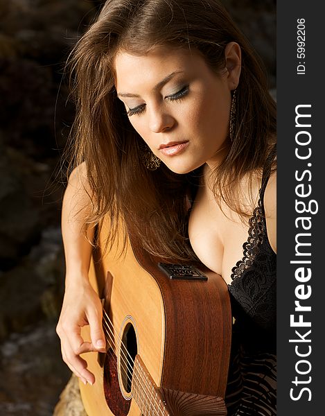 Pretty female singer playing guitar, sitting on the rocks. Pretty female singer playing guitar, sitting on the rocks.