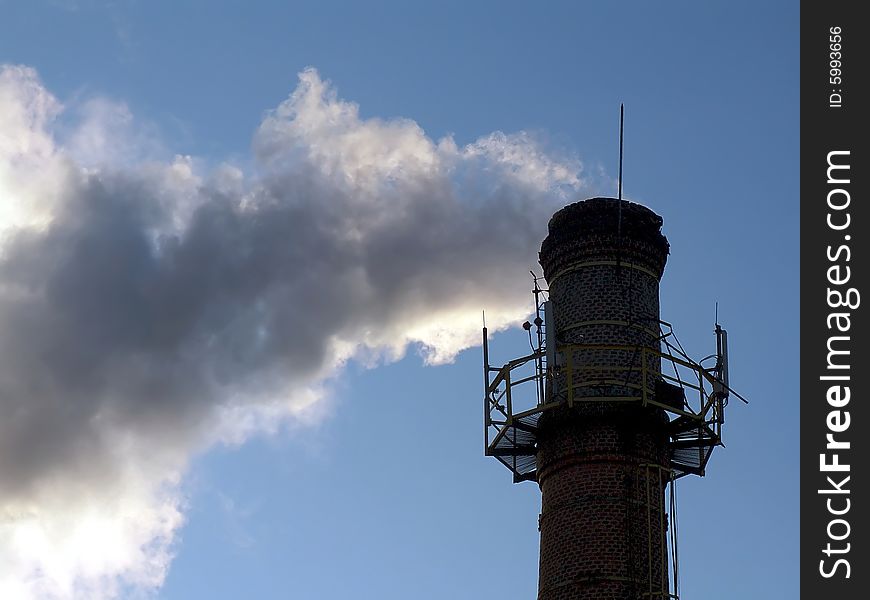 Industrial brick tube with white smoke highlighted by sunset sun. Industrial brick tube with white smoke highlighted by sunset sun.