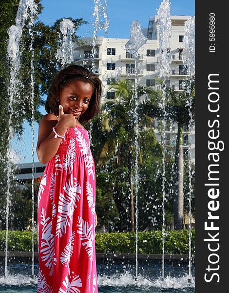 Girl standing with fountains in the background. Girl is smiling and displaying a thumbs-up gesture. Girl standing with fountains in the background. Girl is smiling and displaying a thumbs-up gesture.