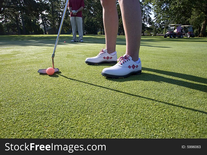 A person is standing on the green of a golf course.  They are about to putt a ball into a hole.  Horizontally framed shot. A person is standing on the green of a golf course.  They are about to putt a ball into a hole.  Horizontally framed shot.