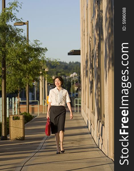 Smiling woman walks toward camera while carrying a red handbag. Horizontally framed photo. Smiling woman walks toward camera while carrying a red handbag. Horizontally framed photo.