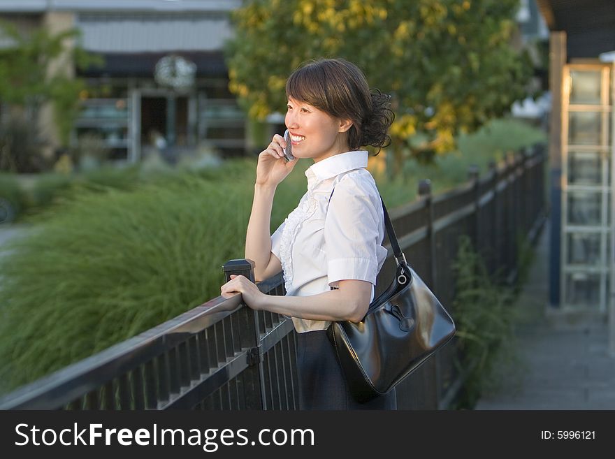 Smiling woman talking on cellphone while leaning over railing. Horizontally framed photo. Smiling woman talking on cellphone while leaning over railing. Horizontally framed photo.