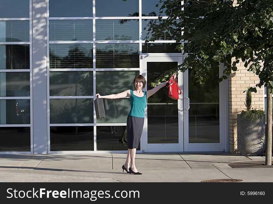 Woman smiles at camera while holding briefcase and red handbag out to her side. Horizontally framed photo. Woman smiles at camera while holding briefcase and red handbag out to her side. Horizontally framed photo.