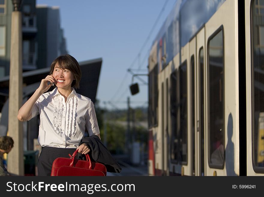 Smiling woman walks while talking on cell phone and holding red handbag. She is walking next to a train. Horizontally framed photo. Smiling woman walks while talking on cell phone and holding red handbag. She is walking next to a train. Horizontally framed photo.